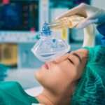 Patient under general anesthesia with an anesthesiologist administering a breathing mask in an operating room.
